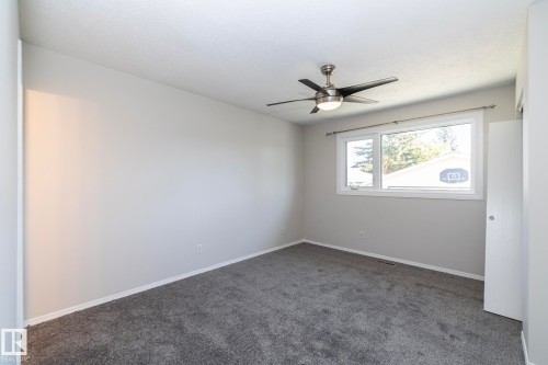 Neutral wall finishes, textured ceiling, gray carpet flooring, window with white trim, and a ceiling fan with integrated lighting - 17311 107 Street Nw, Edmonton, AB 
