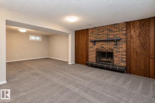 Expansive room featuring a brick fireplace with a tiled hearth and wood paneling - 17311 107 Street Nw, Edmonton, AB 