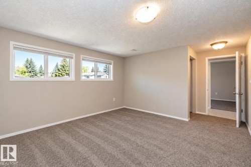 Neutral tone painted walls, textured ceiling, two windows with blinds, wall-to-wall carpeting, and flush mount lighting - 17311 107 Street Nw, Edmonton, AB 