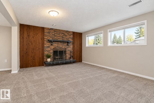 Brick fireplace with a dark mantel, wood paneling, light-colored carpeting, recessed ceiling light, and multiple windows - 17311 107 Street Nw, Edmonton, AB 