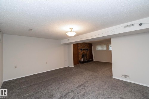 Spacious room with new gray carpeting, white painted walls, and a recessed fireplace with a brick surround - 17311 107 Street Nw, Edmonton, AB 