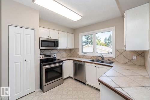 White cabinetry with black hardware, stainless steel appliances, tile flooring, and a double basin sink - 17311 107 Street Nw, Edmonton, AB 