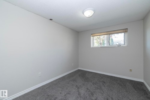 Light gray wall color, textured ceiling, flush mount ceiling light, carpeted flooring, and a single window with blinds - 17311 107 Street Nw, Edmonton, AB 
