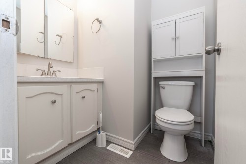 Vanity with integrated sink, wood-finish flooring, wall-mounted mirror, white cabinetry, and toilet with over-the-toilet storage unit - 17311 107 Street Nw, Edmonton, AB 