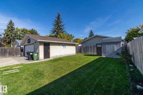 Expansive backyard featuring a detached garage, a storage shed with a shingled roof, a wooden privacy fence, and a concrete driveway - 17311 107 Street Nw, Edmonton, AB 