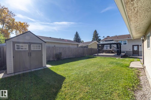 Expansive backyard featuring a lush lawn, wooden privacy fence, storage shed, and a raised deck with a gazebo - 17311 107 Street Nw, Edmonton, AB 