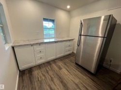 White cabinetry with polished hardware, light-toned countertop, wood-finish flooring, recessed lighting, and a stainless steel refrigerator - 
