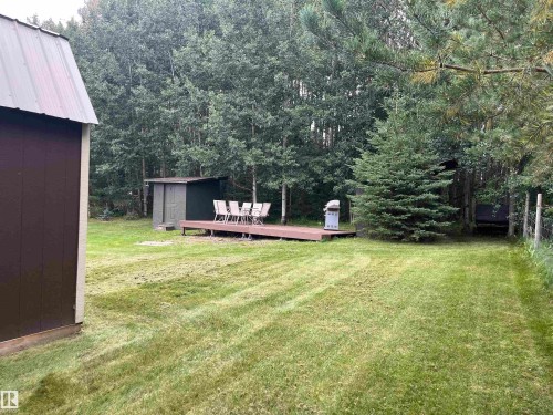 Expansive grassy area featuring a shed with a metal roof, a wood-finish deck, and a secondary small shed - #15 2319 Twp Road 524, Rural Parkland County, AB 
