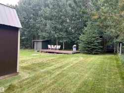 Expansive grassy area featuring a shed with a metal roof, a wood-finish deck, and a secondary small shed - 