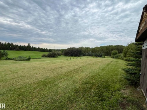 Expansive green lawn with distant tree lines, bordered by natural landscaping and a structure with wood siding - #15 2319 Twp Road 524, Rural Parkland County, AB 