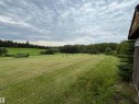Expansive green lawn with distant tree lines, bordered by natural landscaping and a structure with wood siding - #15 2319 Twp Road 524, Rural Parkland County, AB 
