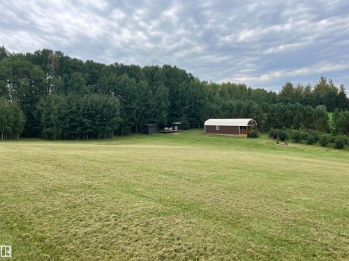 Expansive green space featuring a structure with a brown exterior and white roof, surrounded by mature trees - #15 2319 Twp Road 524, Rural Parkland County, AB 