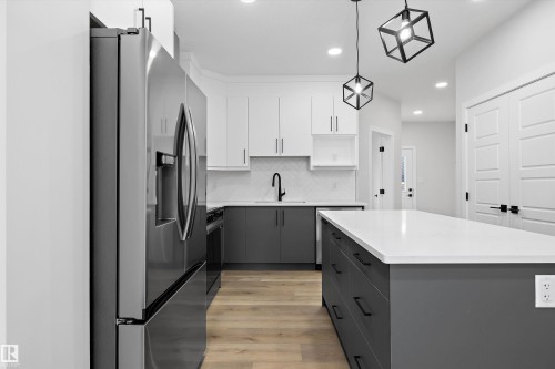 Kitchen featuring two-tone cabinetry, a central island with a solid surface countertop, wood-finish flooring, geometric pendant lighting, and a stainless steel refrigerator - Edmonton, AB 