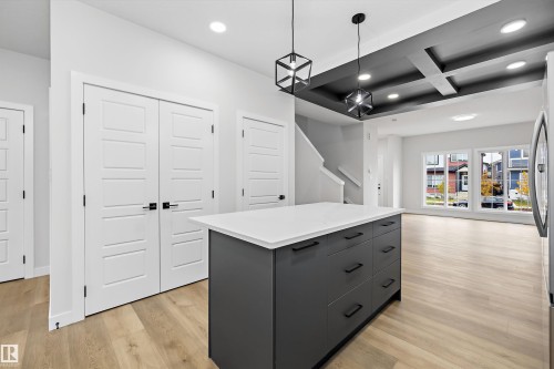 Kitchen island with a solid surface countertop and matte black hardware, coffered ceiling with recessed lighting, wood-finish flooring, and geometric pendant lights - Edmonton, AB 