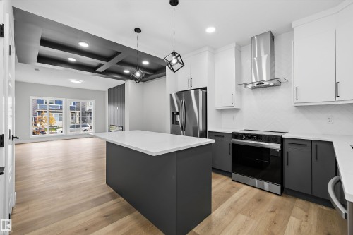 Kitchen featuring a central island with a solid surface countertop, two-toned shaker-style cabinetry, stainless steel appliances, herringbone-patterned wall tile, and wood-finish flooring - Edmonton, AB 