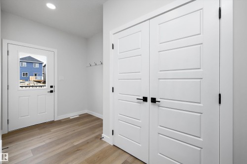 Entry area featuring wood-finish flooring, double-panel closet doors with matte black hardware, a recessed ceiling light, and wall-mounted hooks - Edmonton, AB 
