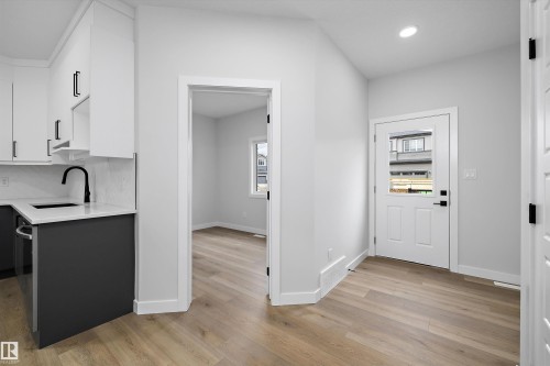 Kitchen featuring two-tone cabinetry, quartz countertops, and matte black plumbing fixtures, paired with wood-finish flooring throughout and a door with an integrated glass panel - Edmonton, AB 