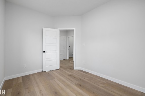 Neutral interior space featuring wood-finish flooring, five-panel doors, and matte black hardware - Edmonton, AB 