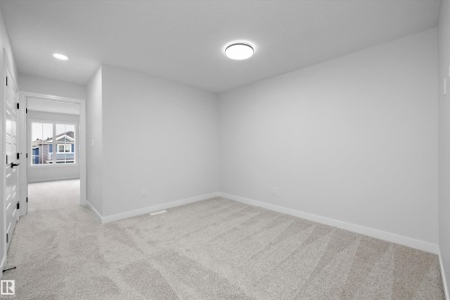 Neutral-toned interior space featuring wall-to-wall carpeting, crisp white walls, a flush-mount circular ceiling light, and a multi-pane window - Edmonton, AB 