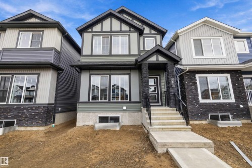 Two-story residence featuring a Tudor-inspired exterior, stone-veneer entryway pillars, concrete steps with metal railings, and multi-pane grid windows - Edmonton, AB 
