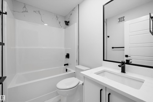 Bathroom featuring a vanity with a white countertop and rectangular undermount sink, black hardware, framed wall mirror, and a shower-tub combination with patterned tile surround - Edmonton, AB 