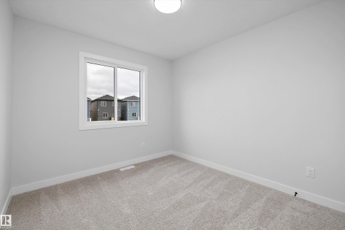 Neutral-toned interior space featuring light grey wall paint, plush neutral carpeting, a dual-pane sliding window, and a central flush-mount ceiling light fixture - Edmonton, AB 