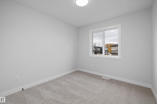 Neutral-toned interior space featuring light-colored wall paint, plush carpeting, a dual-pane sliding window with white trim, and a flush-mount ceiling light fixture - Edmonton, AB 