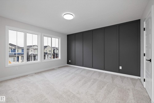 Interior space featuring a dark-toned board and batten accent wall, neutral carpeting, expansive multi-pane windows, and a flush-mount ceiling light fixture - Edmonton, AB 