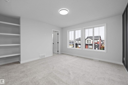 Room featuring neutral carpeting, floor-to-ceiling built-in shelving, dual double-pane windows, and a charcoal-toned accent wall - Edmonton, AB 