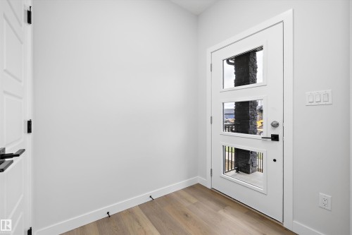 Entryway featuring white walls, wood-finish flooring, and a white door with triple-pane glass inserts and matte black hardware - Edmonton, AB 