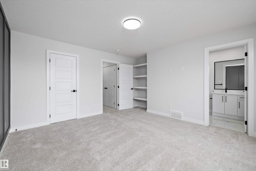 Neutral interior featuring wall-to-wall carpeting, recessed ceiling lighting, built-in open shelving, and solid-core four-panel doors with matte black hardware - Edmonton, AB 