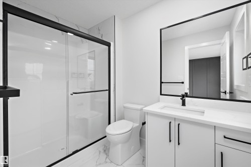 Bathroom featuring a walk-in shower with a glass enclosure, white vanity cabinet with a stone-surface countertop, matte black hardware, and an oversized framed mirror - Edmonton, AB 