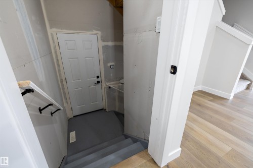Interior stairwell featuring wood-finish flooring, painted six-panel door with matte black hardware, and wall-mounted handrail with black brackets - Edmonton, AB 