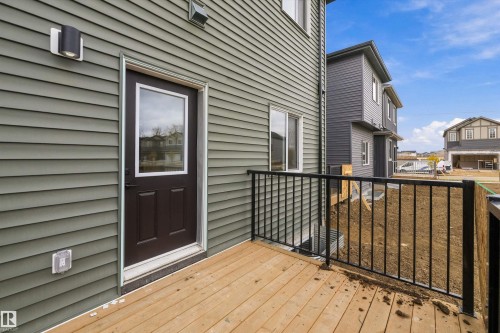 Exterior deck featuring wood-finish decking, black metal railing, olive-toned siding, and a dark-finish entry door with a glass pane - Edmonton, AB 