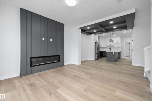 Vertical-plank feature wall with a built-in linear fireplace, coffered ceiling, wood-finish flooring, kitchen island, and recessed lighting - Edmonton, AB 