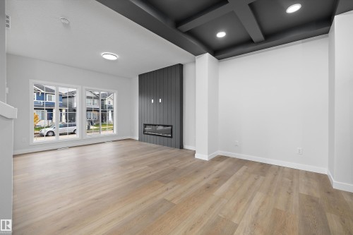 Interior space featuring wood-finish flooring, a coffered ceiling with recessed lighting, and a floor-to-ceiling vertical plank accent wall with a built-in linear electric fireplace - Edmonton, AB 