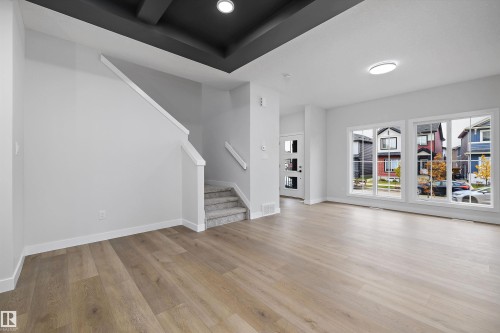 Living area featuring wood-finish flooring, a tray ceiling with recessed lighting, large windows with muntins, and a staircase with a white handrail - Edmonton, AB 