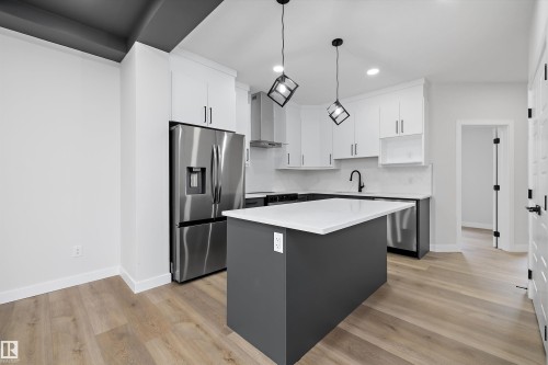 Kitchen featuring white shaker-style cabinetry, stainless steel appliances, a central island with a solid-surface countertop, matte black fixtures, and wood-finish flooring - Edmonton, AB 