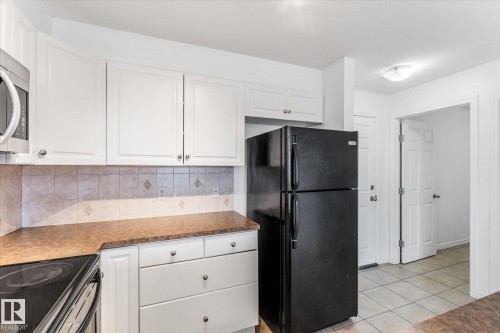 Kitchen featuring white cabinetry, contrasting countertops, a tiled backsplash with diamond accents, and tile flooring - #109 4309 33 St, Stony Plain, AB 