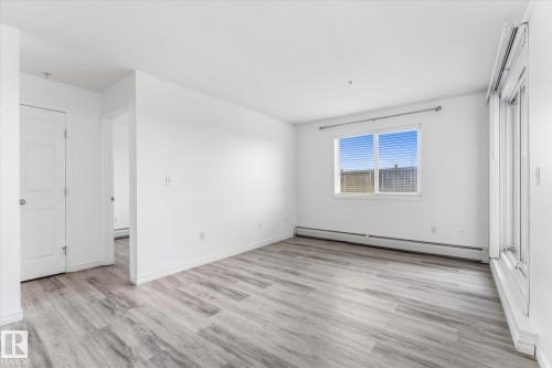 Neutral-toned room featuring wood-finish flooring, a glass sliding door, and a horizontal window with adjustable blinds - #109 4309 33 St, Stony Plain, AB 