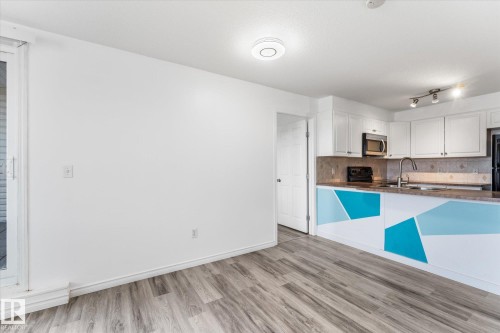 Wood-finish flooring, white shaker-style cabinetry, kitchen peninsula with geometric accents, stone-composite countertop, and sliding glass door - #109 4309 33 St, Stony Plain, AB 