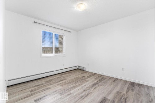 Neutral-toned wood-finish flooring, sliding window with horizontal blinds, flush-mount ceiling light fixture, and white interior walls - #109 4309 33 St, Stony Plain, AB 
