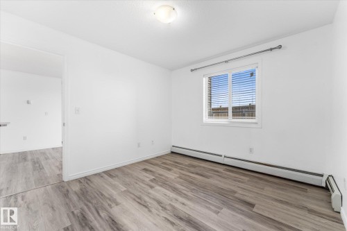 Interior room featuring wood-finish flooring, white walls, a central flush-mount ceiling light, and a horizontal sliding window with metal curtain hardware - #109 4309 33 St, Stony Plain, AB 