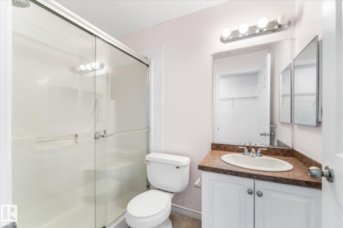 Bathroom featuring a glass-enclosed shower stall with a molded seat, a white vanity cabinet with a stone-finish countertop, an integrated oval sink, and a multi-bulb vanity light fixture - #109 4309 33 St, Stony Plain, AB 