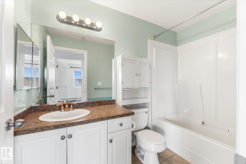 Bathroom featuring a white vanity with a solid-surface countertop, integrated basin, built-in over-the-toilet storage cabinetry, and a full-width vanity mirror with integrated four-light fixture - #109 4309 33 St, Stony Plain, AB 