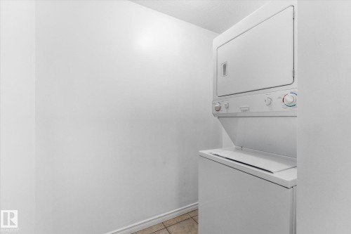 Stacked white laundry appliance set featuring a front-loading washer and top-mounted dryer with neutral tile flooring - #109 4309 33 St, Stony Plain, AB 