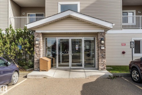 Entrance featuring a gable roof, stone-veneer pillars, glass double doors, and balcony railings - #109 4309 33 St, Stony Plain, AB 