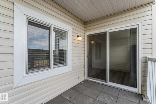 Covered balcony featuring horizontal lap siding, square tile flooring, a sliding glass door, and exterior wall-mounted lighting - #109 4309 33 St, Stony Plain, AB 