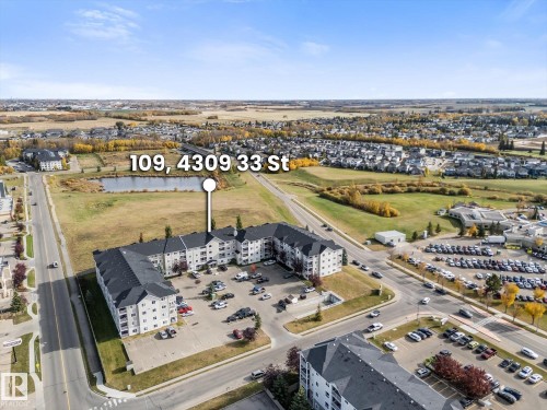 Aerial perspective of a multi-story residential building featuring an asphalt-shingle roof, structured parking lot, and proximity to a retention pond and open green space - #109 4309 33 St, Stony Plain, AB 