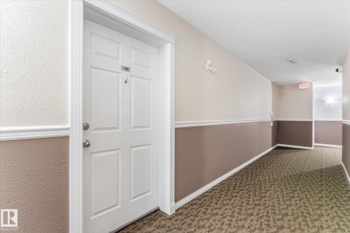 Interior hallway featuring two-tone wall paint, decorative chair rail molding, a six-panel door with metallic hardware, and patterned wall-to-wall carpeting - #109 4309 33 St, Stony Plain, AB 